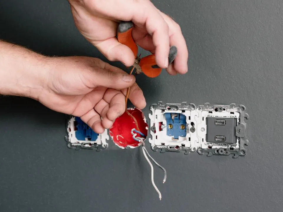 Een elektricien bevestigt met een tang een stopcontact in een grijze wand