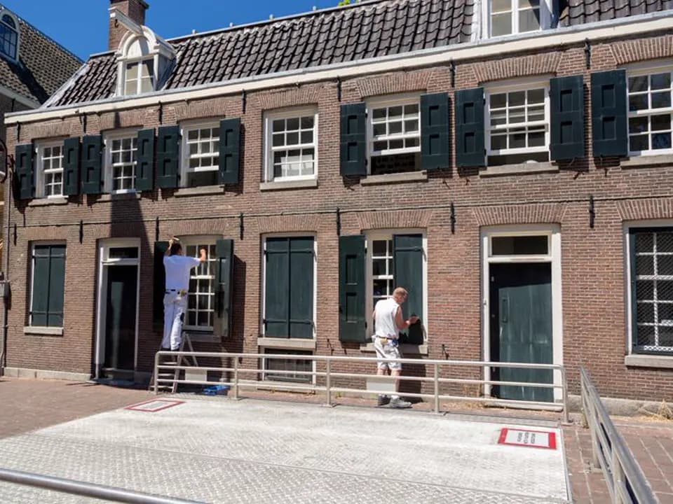 Twee schilders op ladders schilderen de kozijnen van een oud bakstenen pand