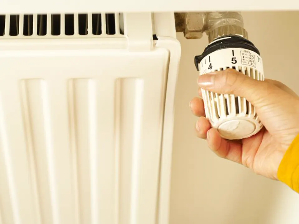 Een hand zet de thermostaatkraan van een witte radiator open