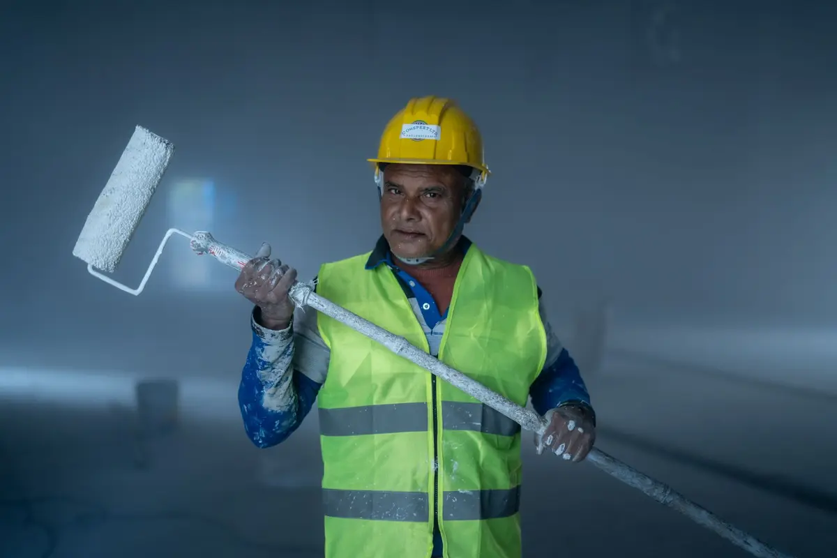 Schilder met helm en verfroller kijkt in de camera