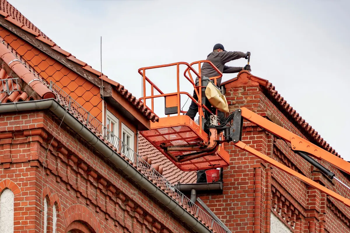 Vakman op een hoogwerker werkt aan een pannendak, met op de voorgrond een dakgoot langs de dakrand