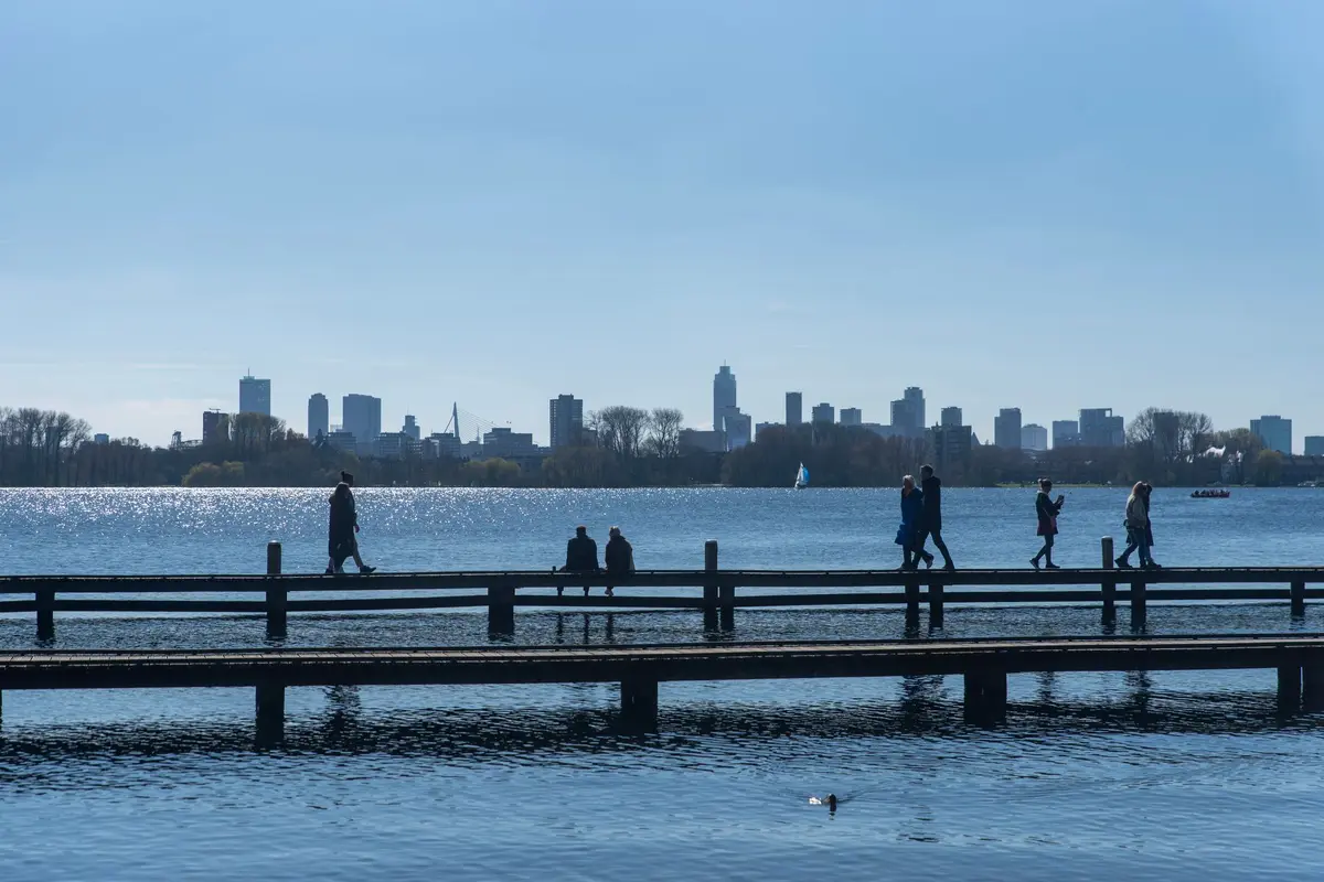 Mensen op een steiger aan de Kralingse Plas, met de skyline van Rotterdam